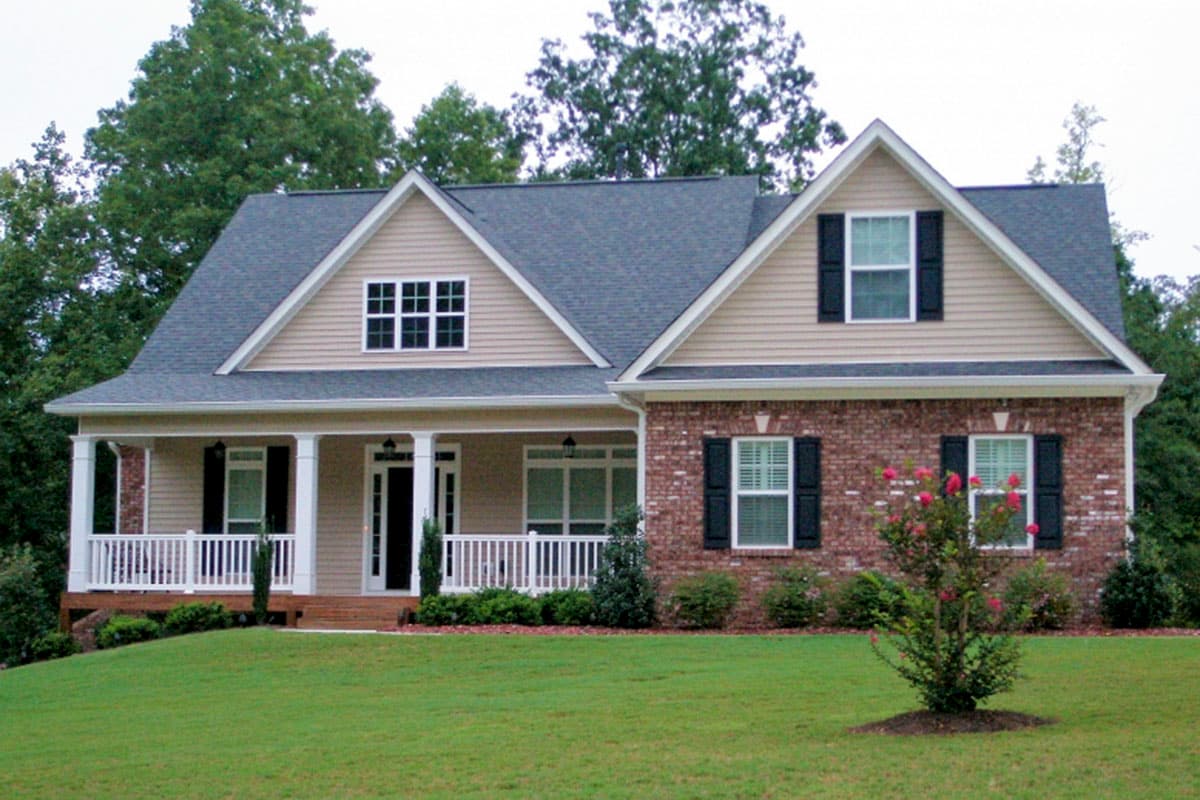 House plan exterior: Two-story home with wraparound porch, gables, dormer, and brick accents.