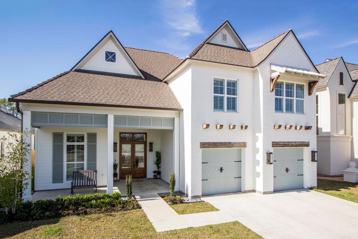 Two-story Modern Farmhouse exterior with a covered front porch, dual garage doors, dormers, and brick facade.