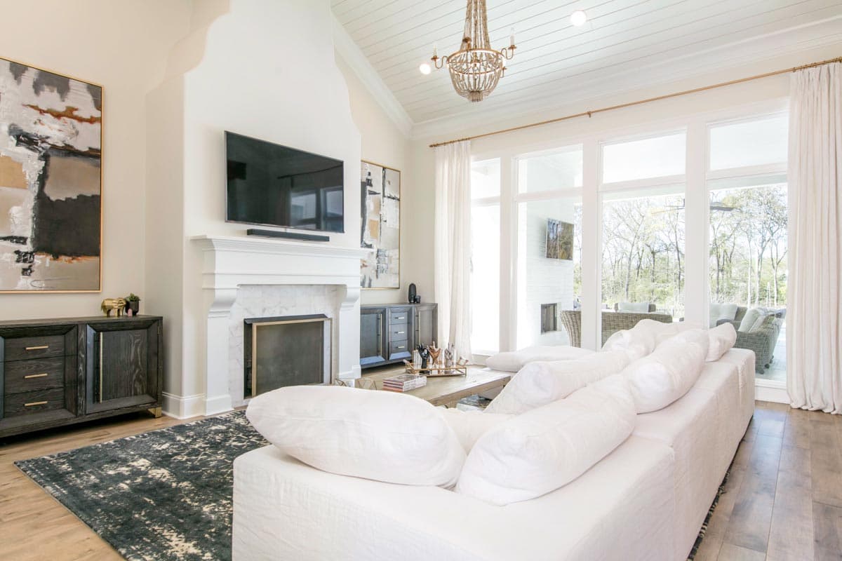 Living room interior with vaulted ceiling, fireplace, large windows, and white sectional sofa.