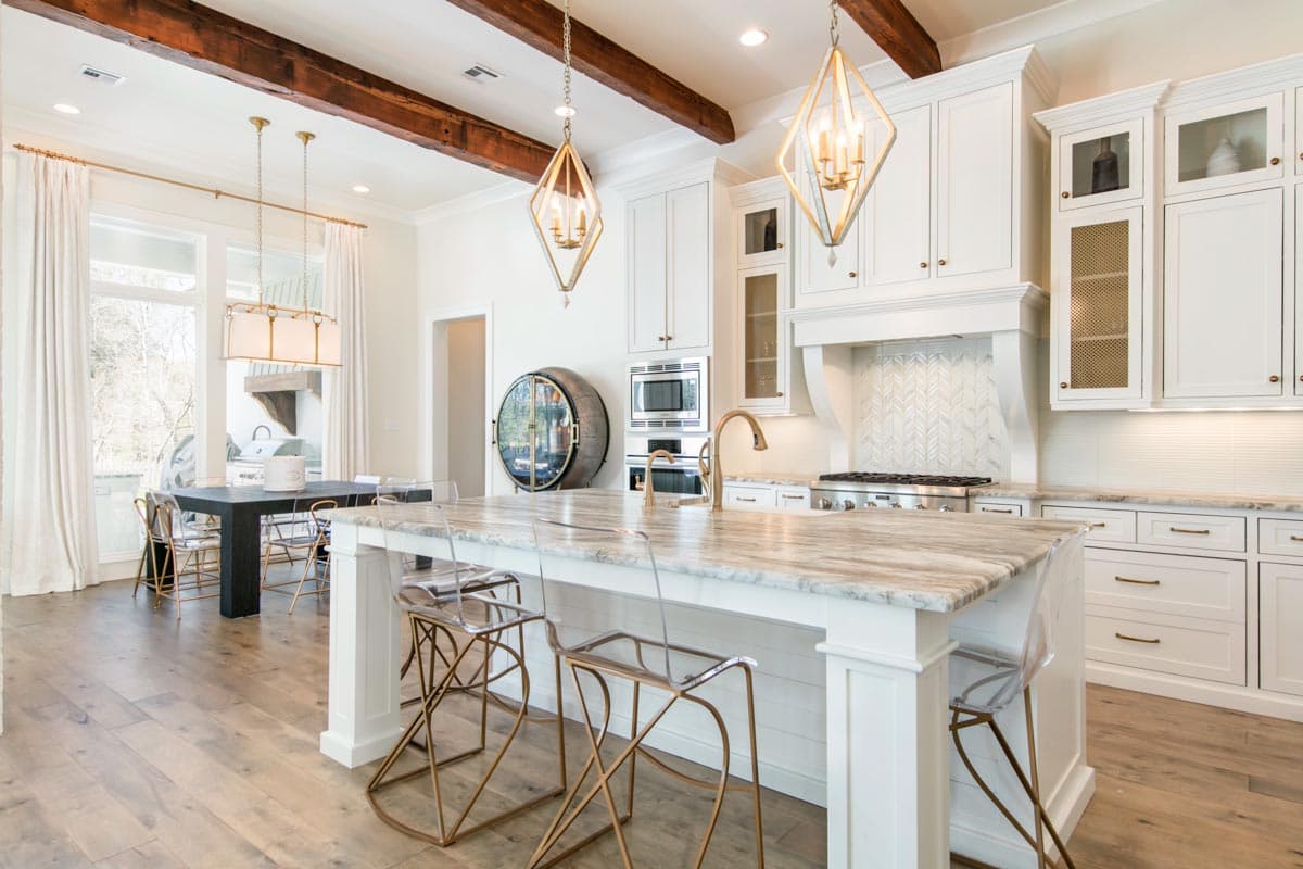 Kitchen with large island, vaulted ceiling with exposed beams, white cabinetry, and stainless steel appliances.