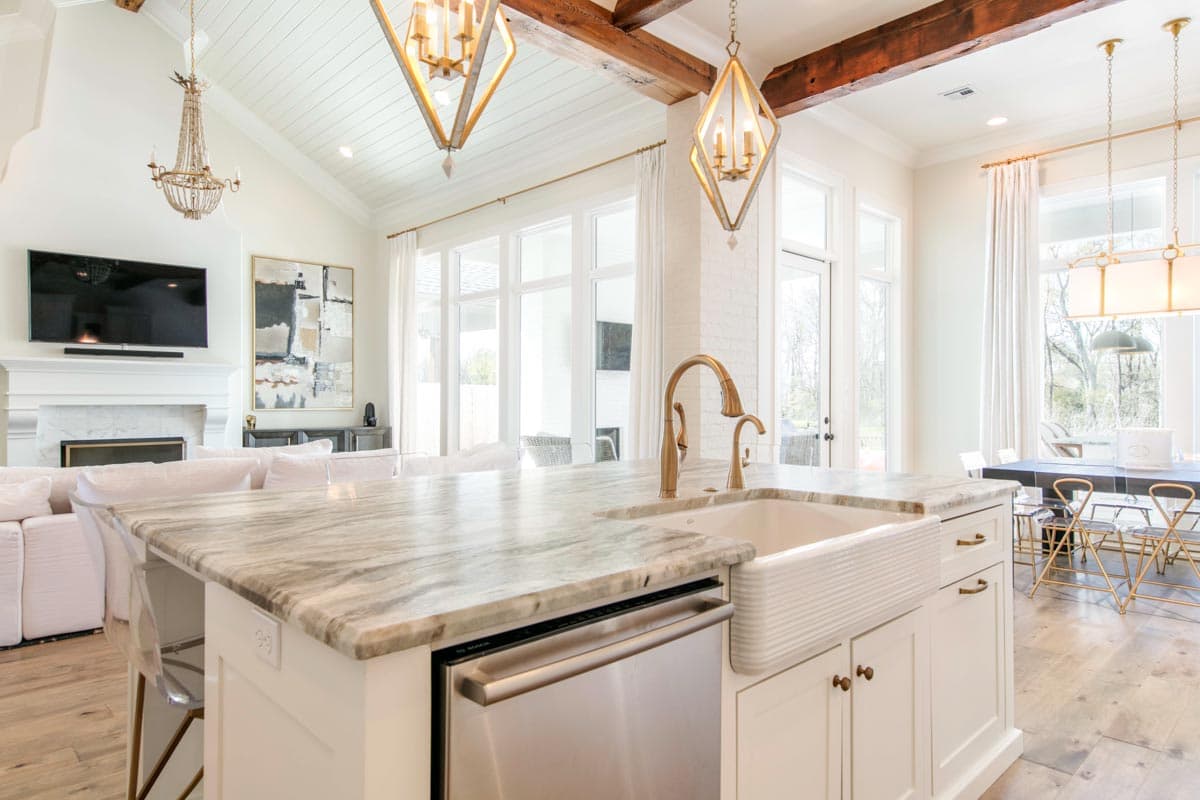 Kitchen with vaulted ceiling, exposed beams, island with marble countertop, farmhouse sink, and fireplace in adjacent great room.