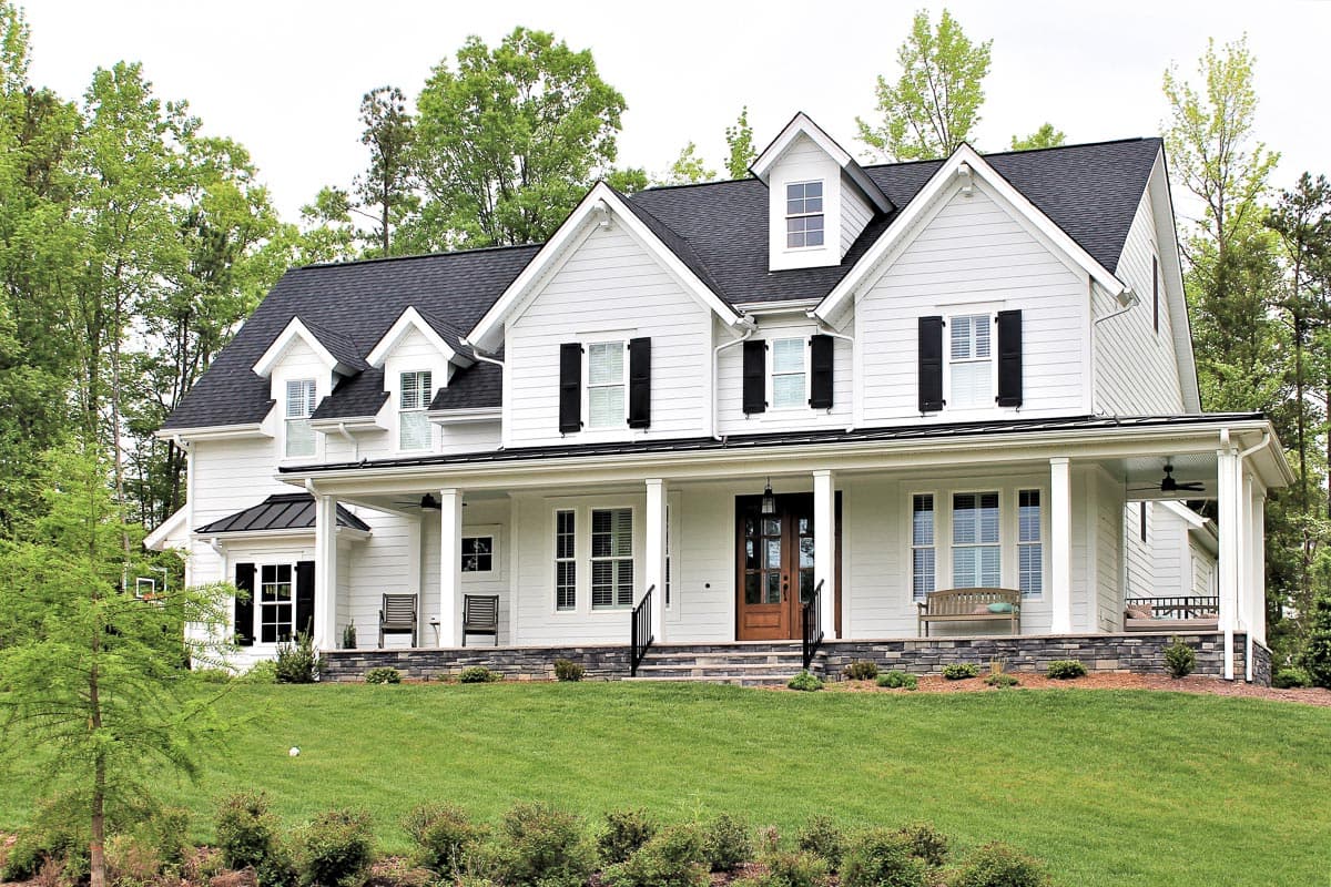 House plan exterior. Two-story Modern Farmhouse with a large front porch, multiple gables, and dormers. Black shutters and dark roof.