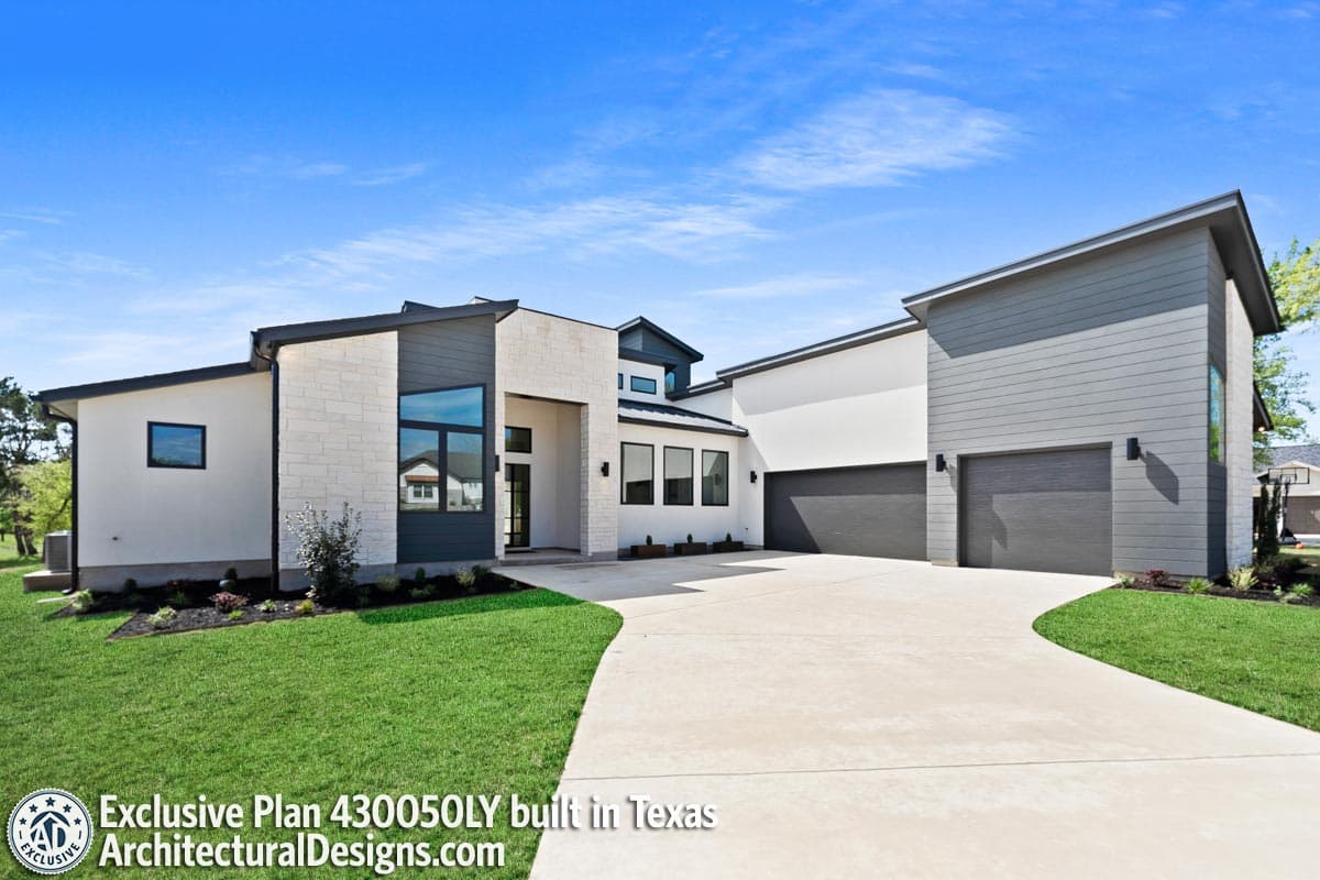 Modern house plan exterior with stone and wood siding, flat rooflines, large windows, and a three-car garage.