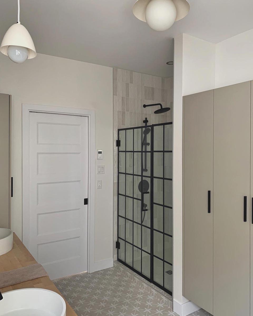 Modern bathroom featuring a glass shower enclosure with black framing, complemented by neutral tones and patterned floor tiles.