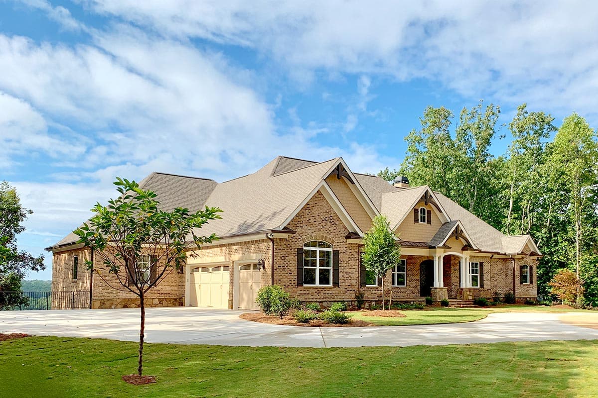 House plan exterior with brick facade, multi-gabled roof, and arched window. Features include a front porch with columns and a three-car garage.