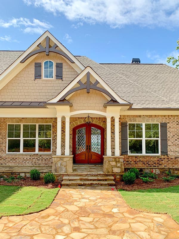 Craftsman style house plan exterior with stone accents, double front doors, gabled dormer with arched window, and decorative timber brackets.