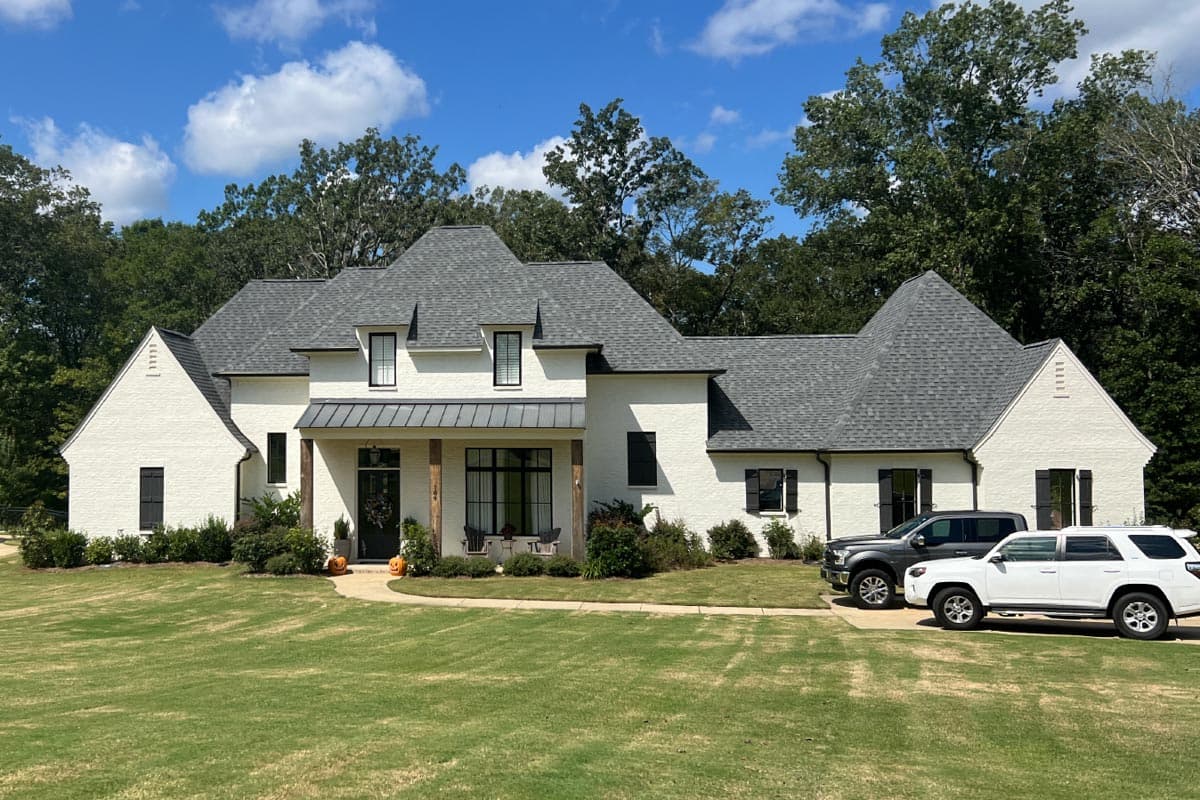 House plan exterior. Two-story, white-brick house with a covered porch and gabled roofline. Includes dormers and black window shutters.