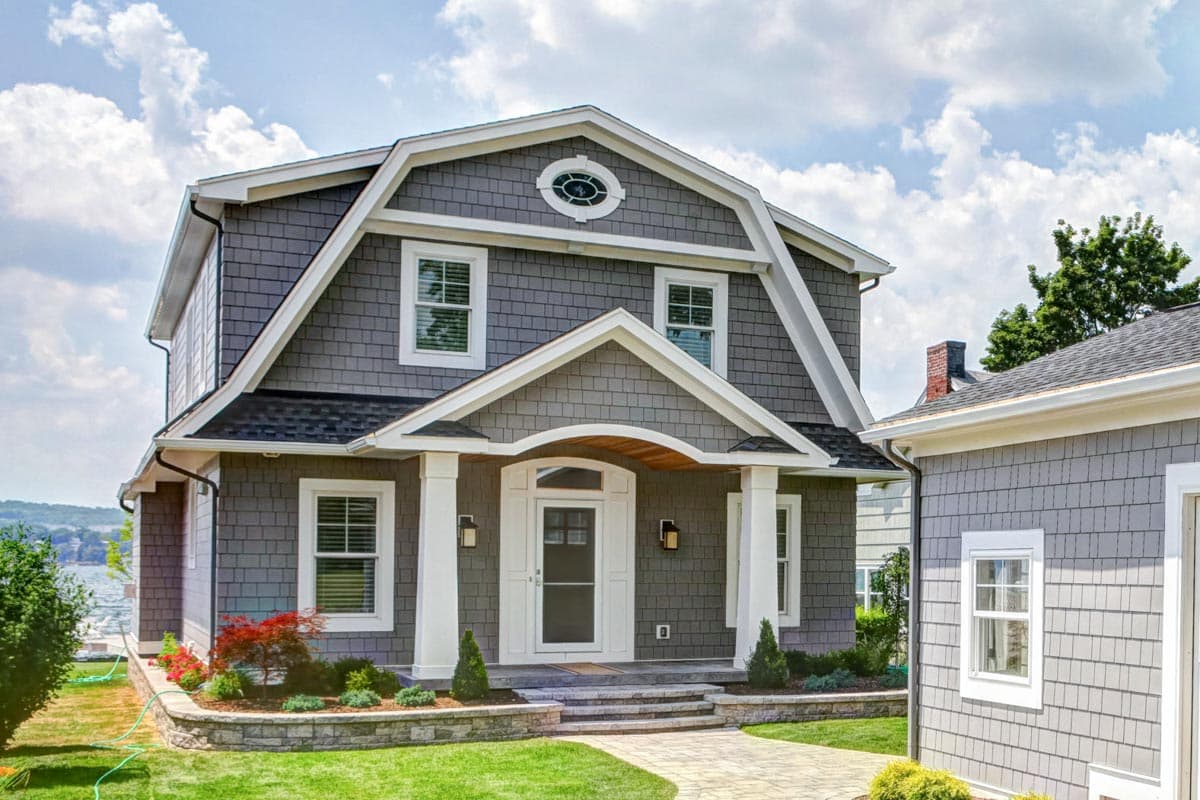 House plan exterior featuring a gambrel roof, centered entrance with arched portico, and shingle siding.