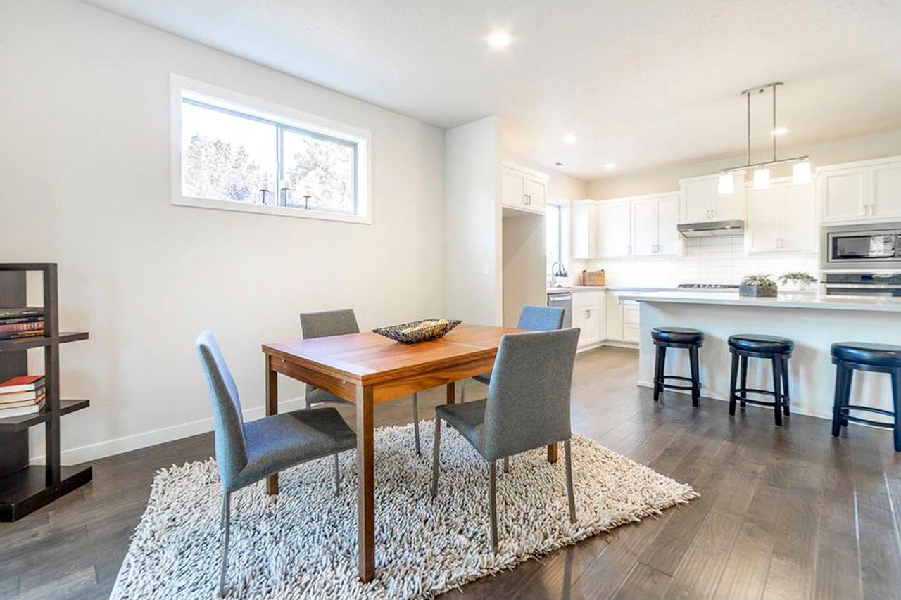 Dining area with wood table and chairs adjacent to kitchen with island, white cabinets, and stainless steel appliances.