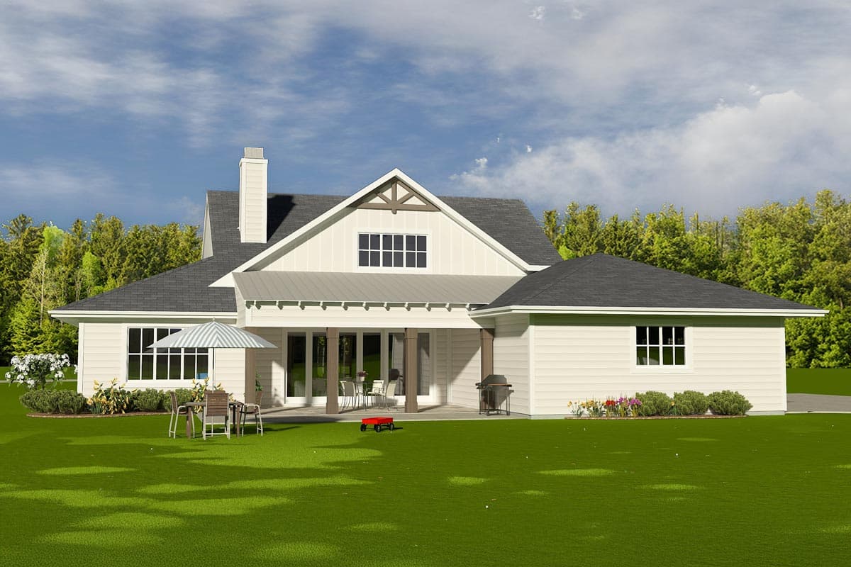 A modern farmhouse with a wraparound porch and a lush green lawn, featuring outdoor seating, a grill, and a red wagon, with trees in the background.