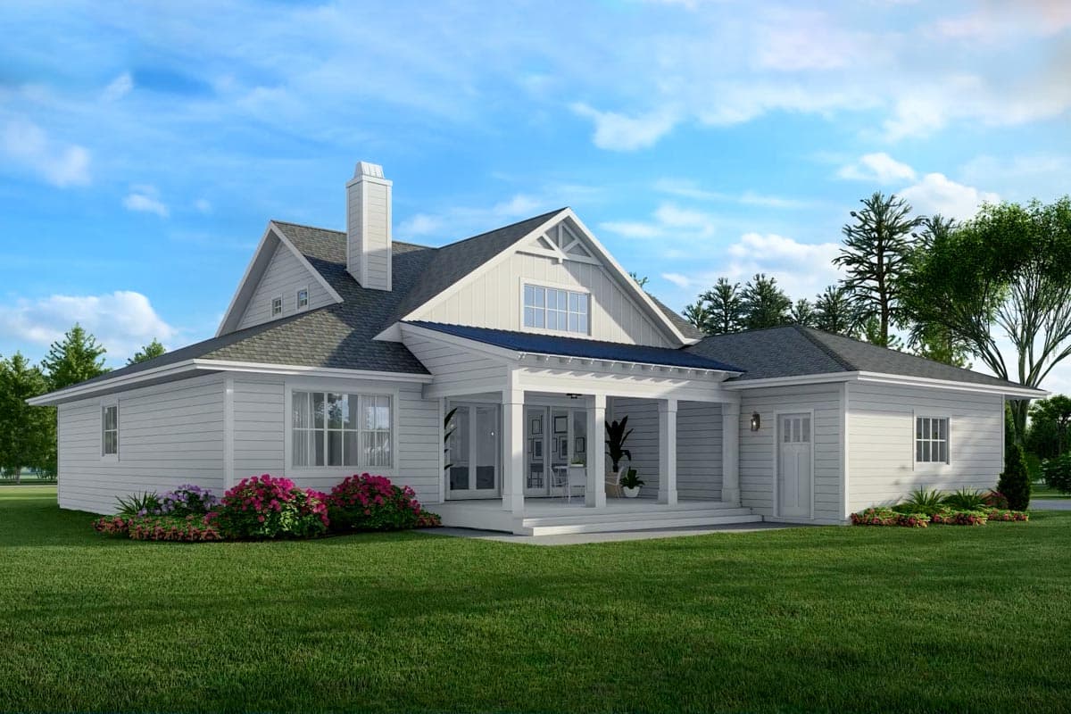 A white, two-story house with a covered porch and manicured lawn. Pink flowers and green trees frame the structure against a blue sky.