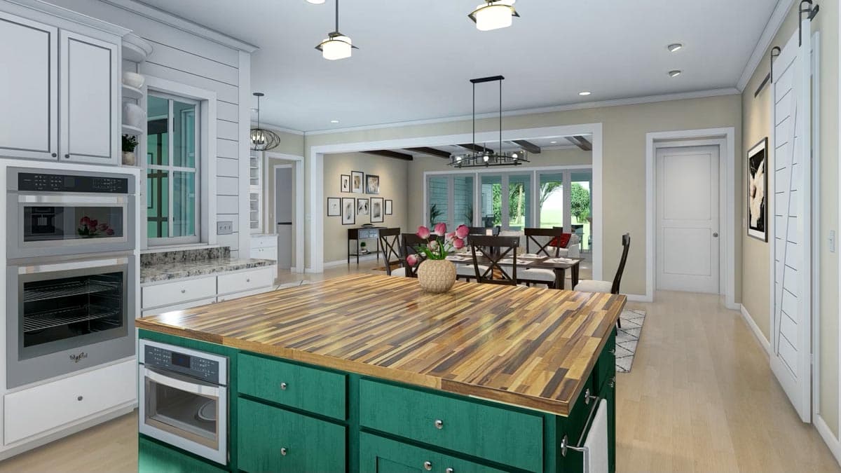 A modern kitchen with a large island with a wood countertop and teal cabinets, facing a dining room with a table set for a meal.