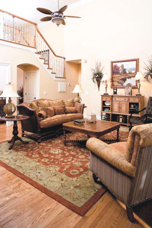 Interior rendering of a living room with a two-story staircase, vaulted ceiling, decorative rug, and traditional furniture.