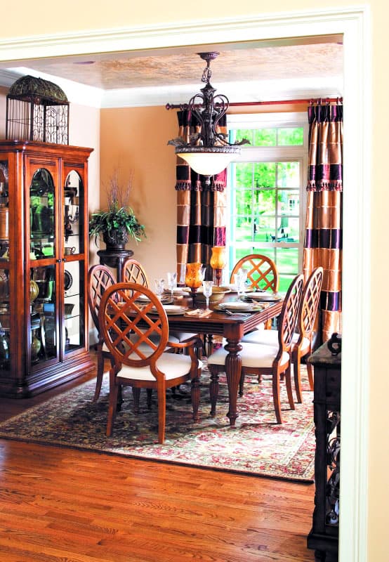 Dining room with wood table, ornate chairs, glass cabinet, patterned rug, and chandelier.
