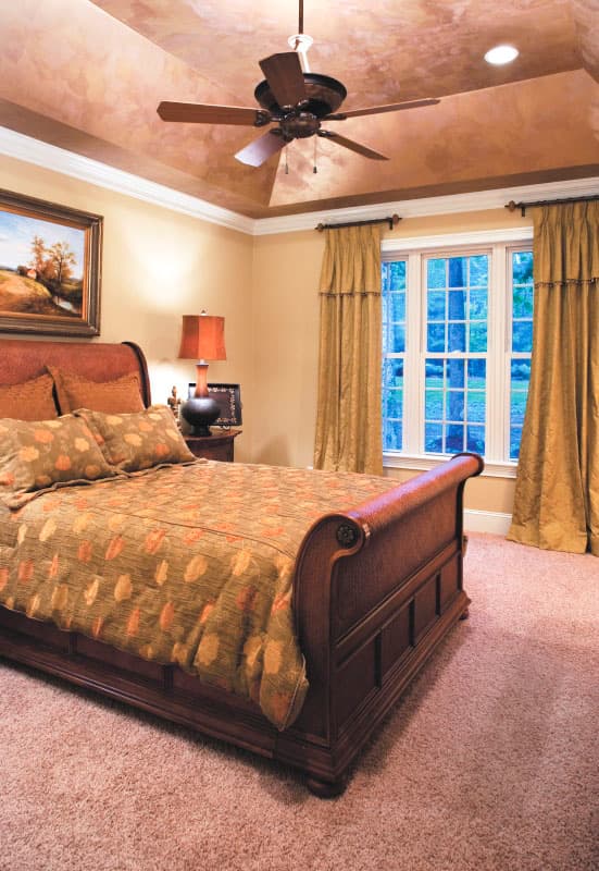 Bedroom with tray ceiling, ceiling fan, large window with grilles, and sleigh bed.