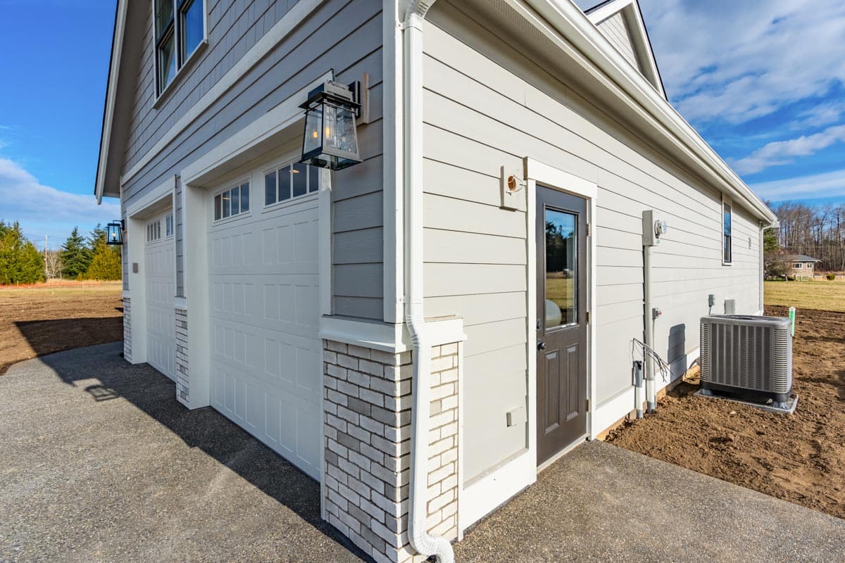House plan exterior shows a two-car garage with paneled doors, decorative brick base, and a side entry door.