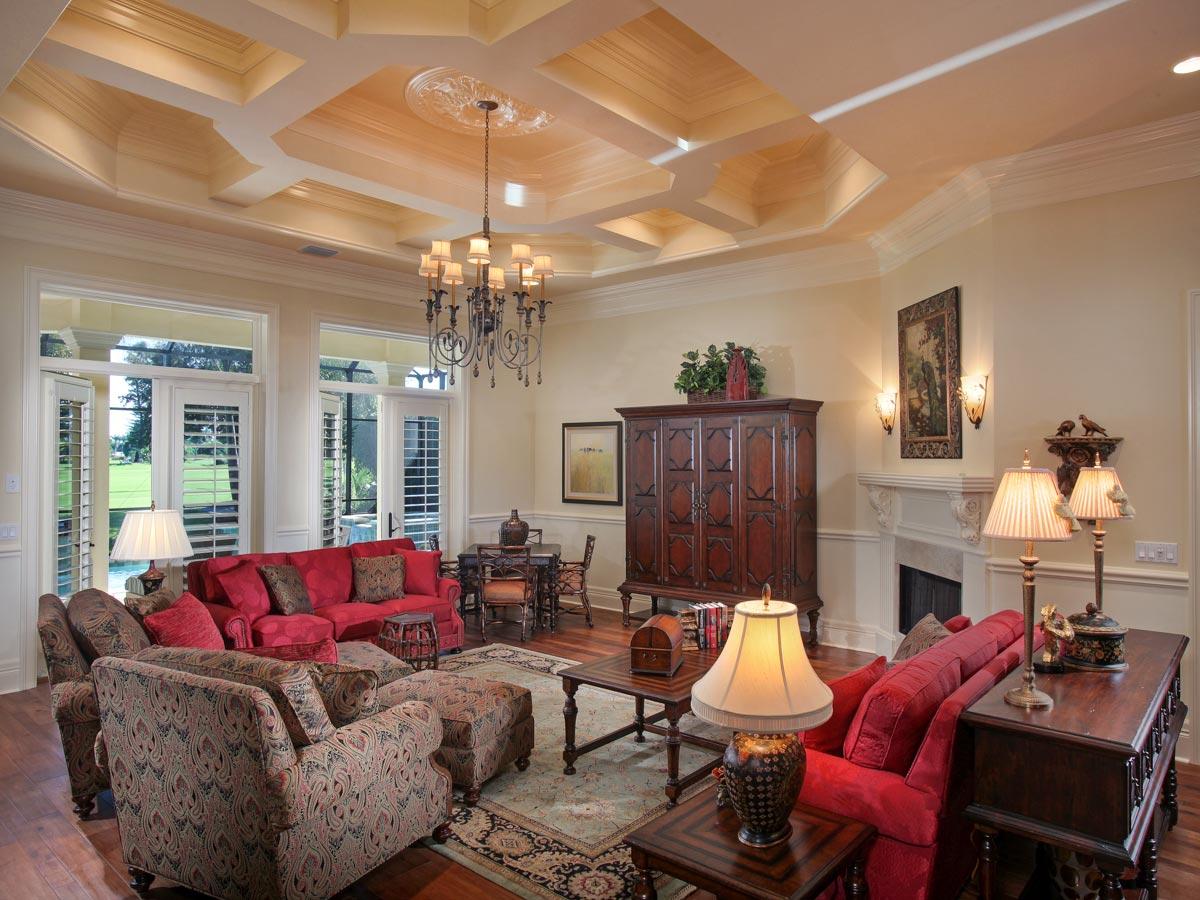Living room with tray ceiling, fireplace, large windows, and French doors. Furnished with red sofas and patterned armchairs.