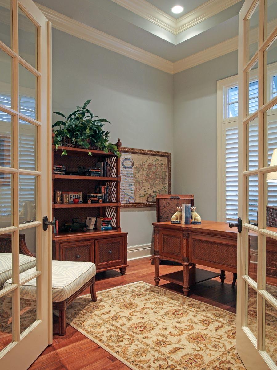 Office with double glass doors, bookshelf, desk, and patterned rug.