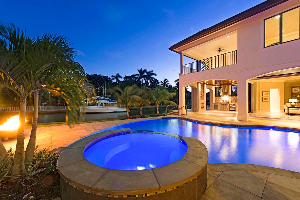 Two-story house exterior with balcony, covered outdoor kitchen, pool, spa, and canal with boat.