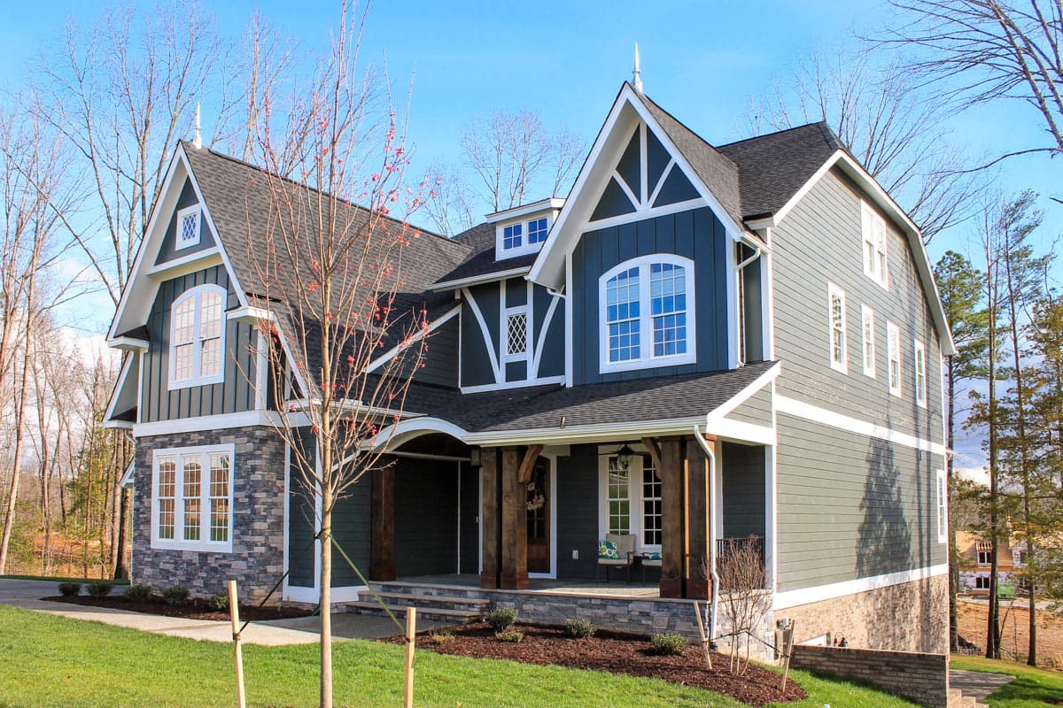 House plan exterior: Two-story Modern Farmhouse with multiple gables, arched windows, stone accents, and a covered porch with timber posts.
