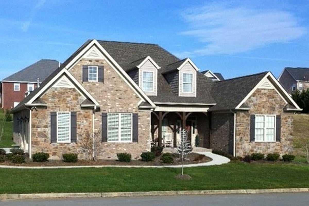 House plan exterior: Two-story home with stone and brick facade, prominent gables, dormers, and a covered front porch with wood supports.