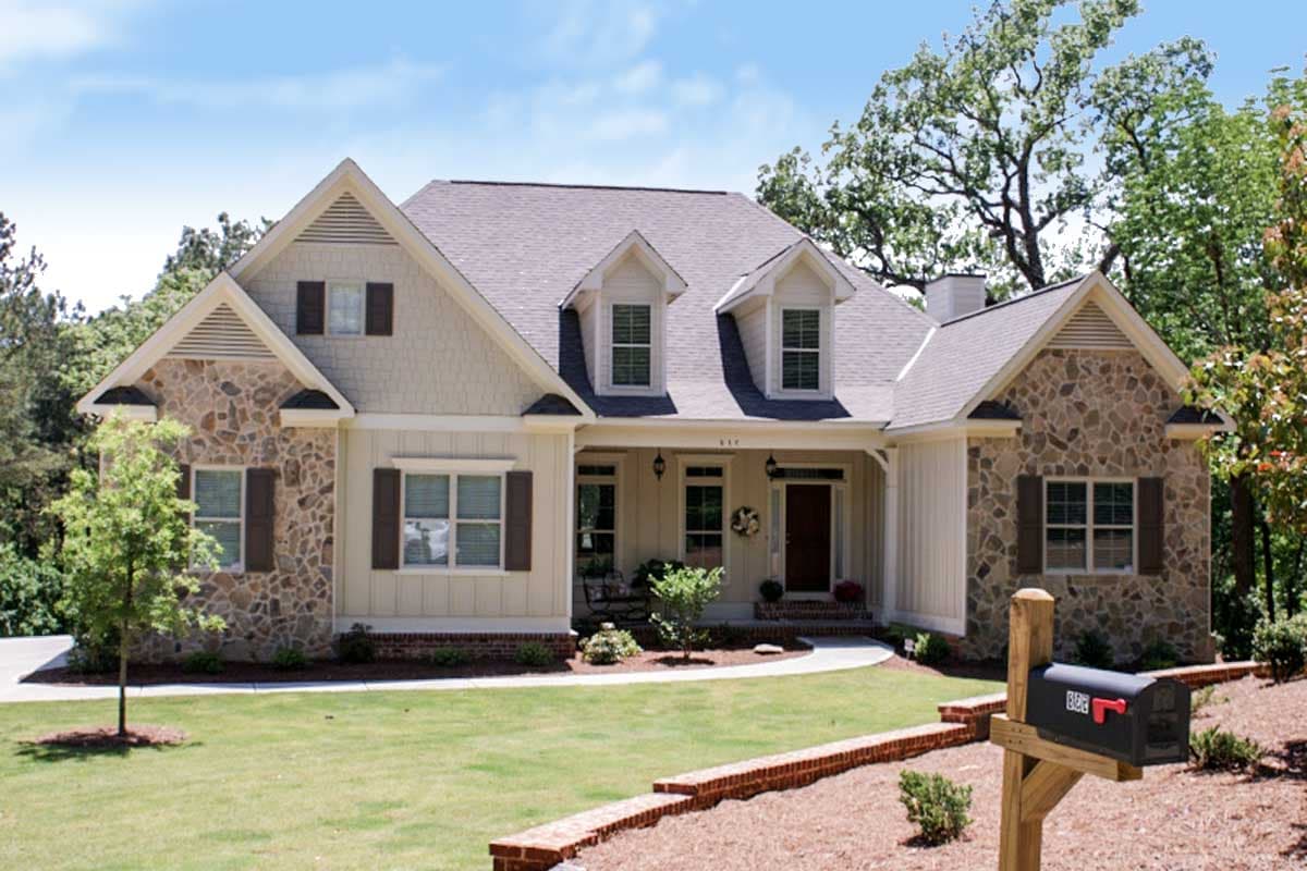 House plan exterior with stone accents, dormers, and a covered porch. Gable roof and multiple window styles are visible on this two-story house.