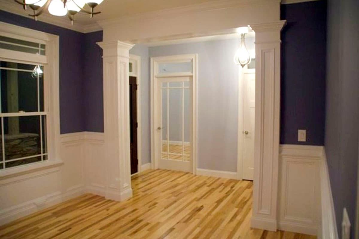 Interior view shows a room with hardwood floors, a window, and a cased opening with decorative columns leading to a hallway with doors.