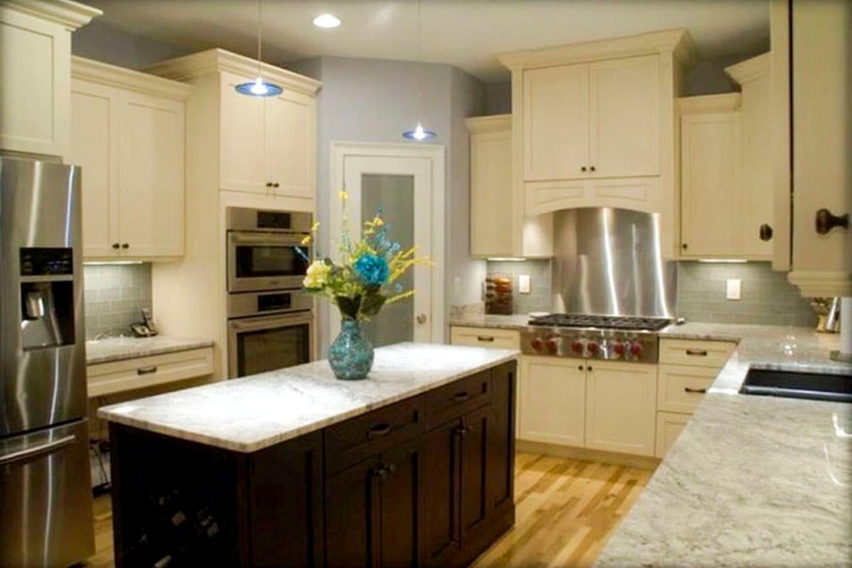 Kitchen with cream cabinets, stainless steel appliances including double ovens and a range, island with dark wood base, and granite countertops.