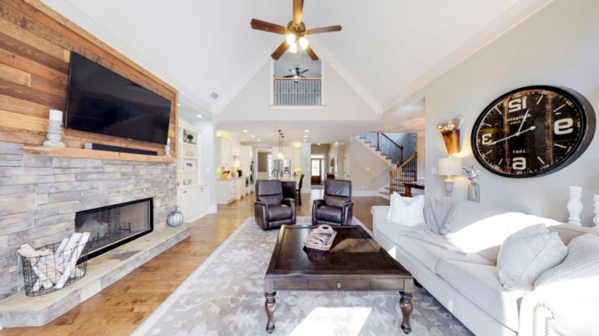 Great room with stone fireplace, wood accent wall, vaulted ceiling, and view of kitchen and staircase.