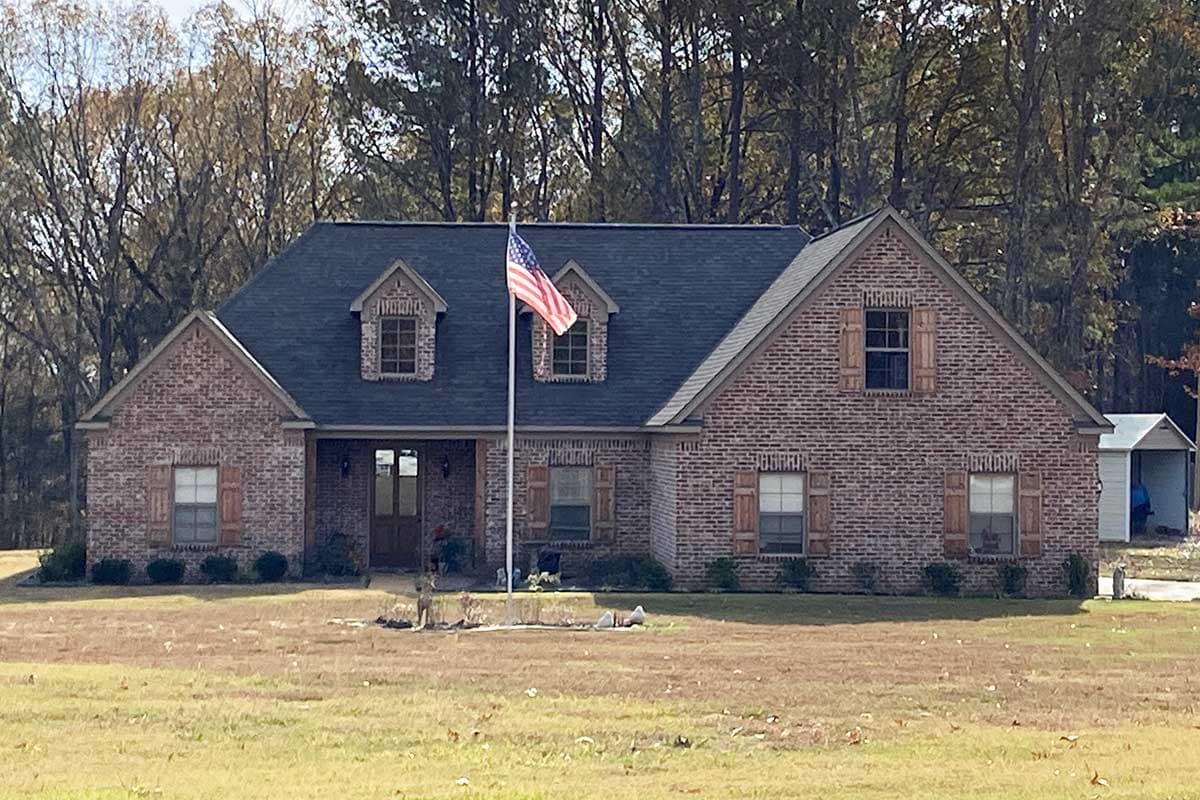 Two-story brick house plan with gables, dormers, and wooden shutters. Features a prominent front porch with double doors.