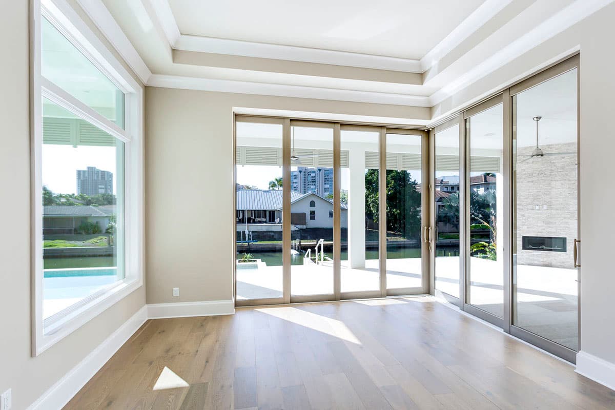 Interior view of a room with a coffered ceiling, large windows, and sliding glass doors opening to a waterfront view.