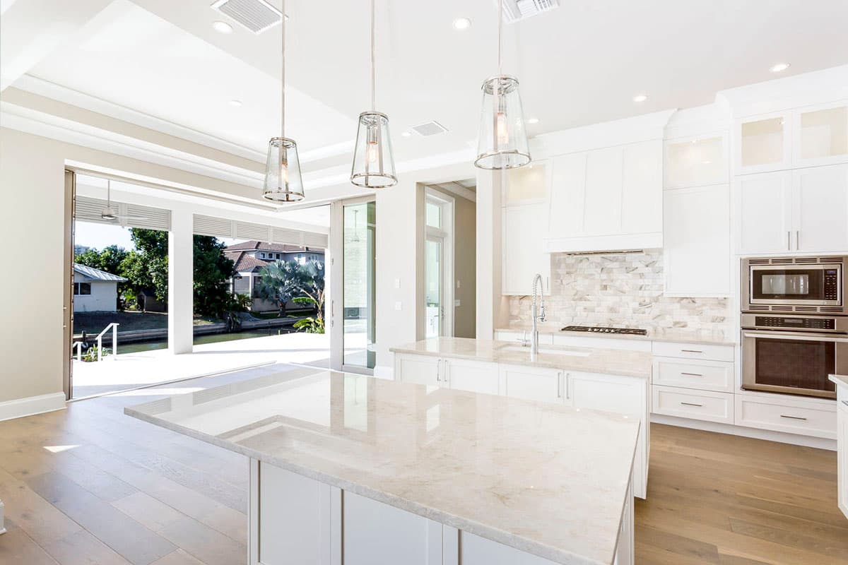 Contemporary kitchen with dual islands, white cabinetry, marble backsplash, and large sliding glass doors opening to a waterfront view.