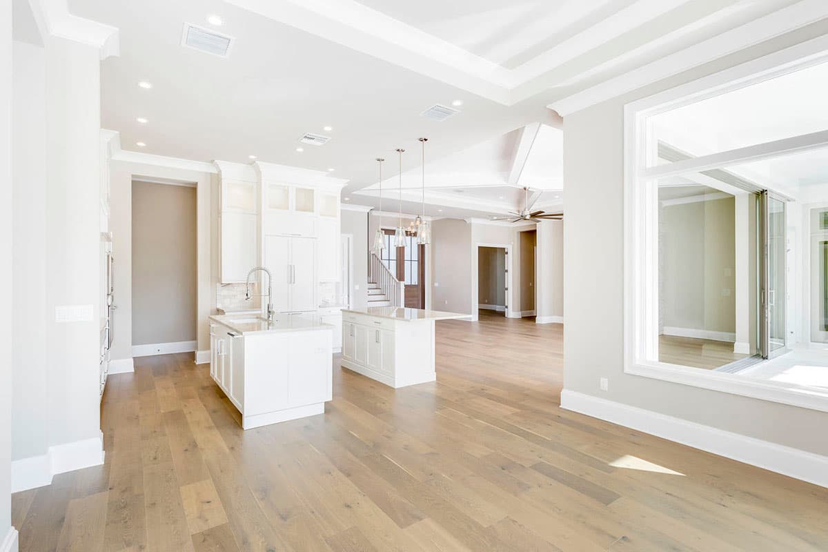 Modern open-concept interior view with white kitchen island, coffered ceiling, and large windows.