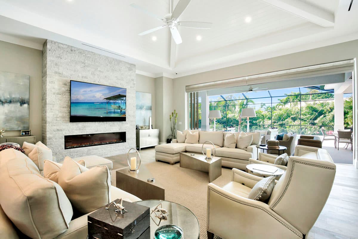 Living room interior with stone fireplace, television, sectional sofa, and sliding glass doors leading to an outdoor patio.