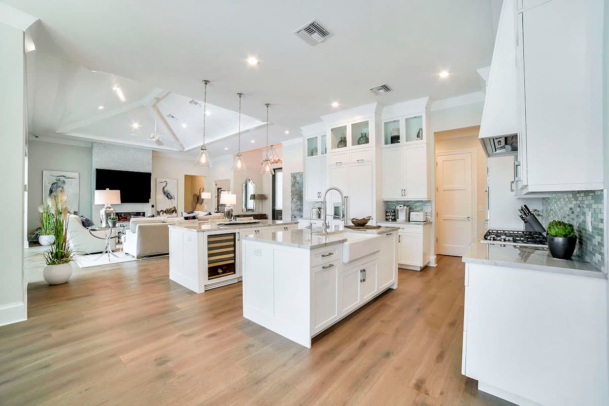 Modern open-concept kitchen with two islands, white cabinetry, farmhouse sink, and adjacent living area with vaulted ceiling.