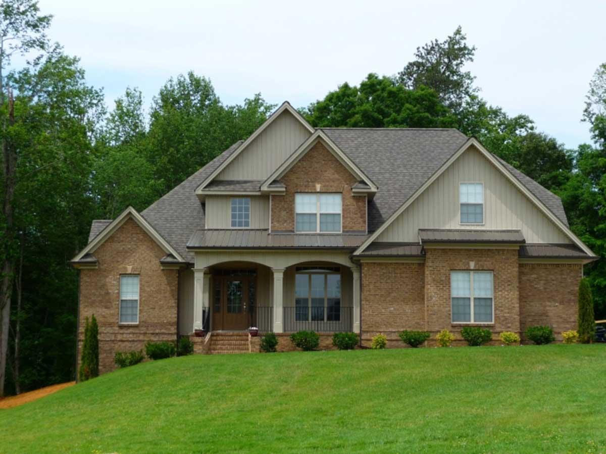 House plan exterior: Two-story brick home with covered front porch, multiple gables, and dormer windows.