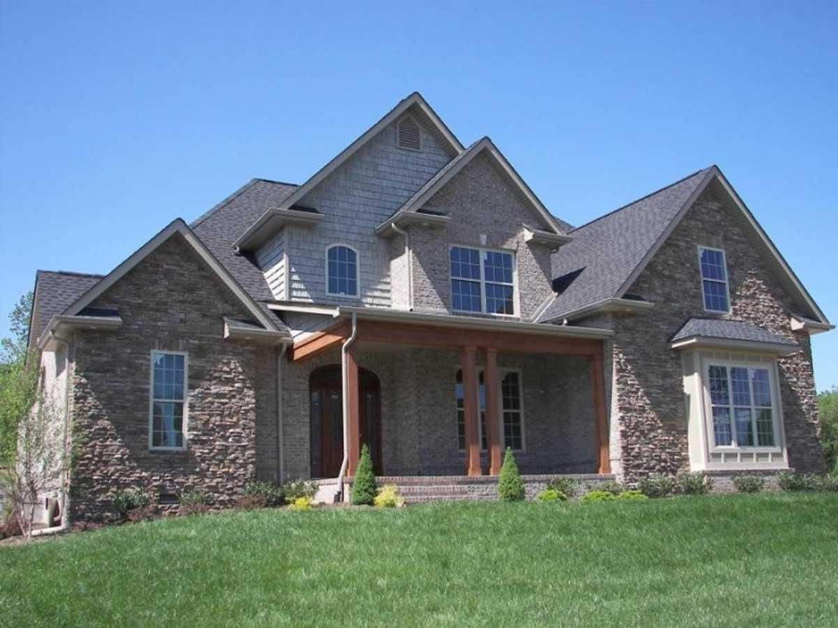 House plan exterior showing a two-story home with stone facade, gabled dormers, and a covered front porch with timber columns.