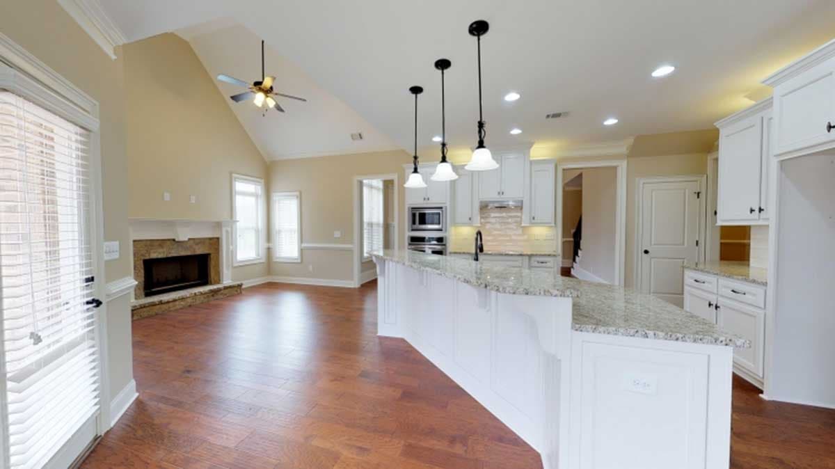 Interior view of open concept living space with vaulted ceiling, stone fireplace, kitchen island with pendant lights, and white cabinetry.