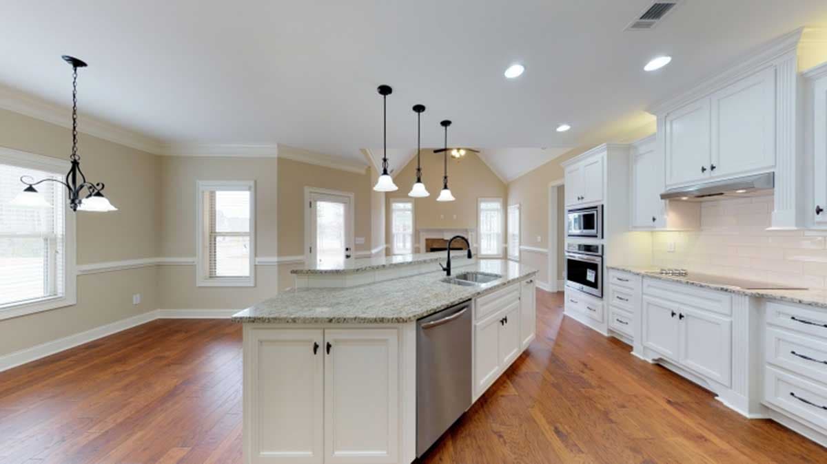Kitchen with island, stainless steel appliances, white cabinetry, granite countertops, and open access to a great room with fireplace.