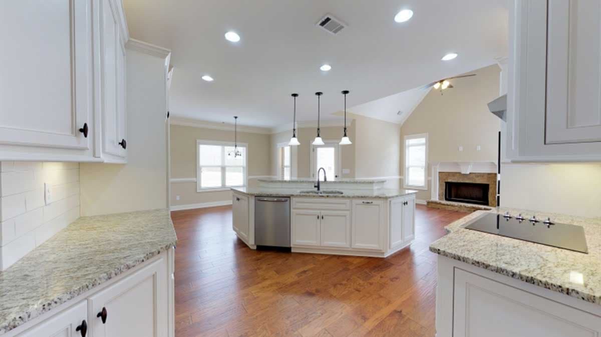 Kitchen with island, sink, dishwasher, and granite counters, opening to a great room with fireplace.