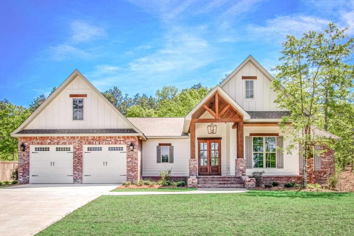 House plan exterior with two-car garage, gable roof, and a front porch with exposed timber framing and brick accents.
