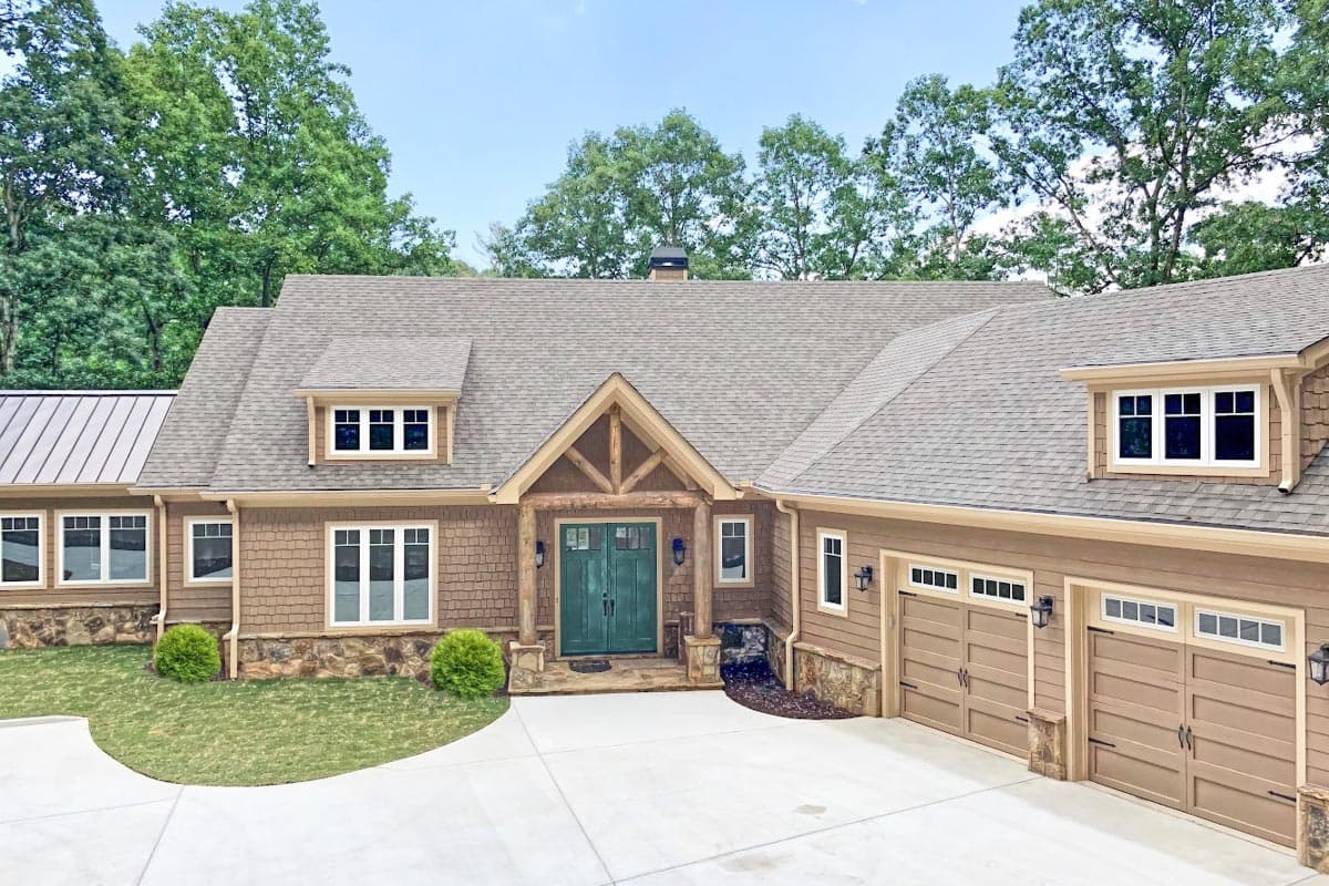 House plan exterior: Craftsman style, one story, prominent gable entry with timber details, three-car garage, dormer windows.