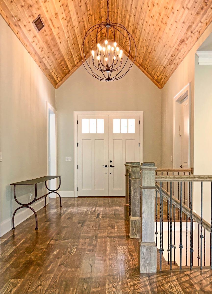 Interior view of foyer with double doors, vaulted wood ceiling, chandelier, and staircase with metal spindles.