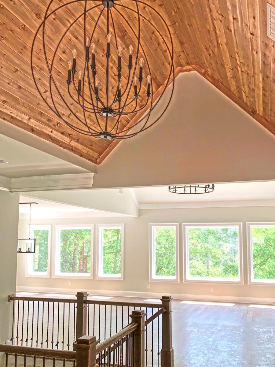 Interior view of an open-concept living space with a vaulted wood-paneled ceiling, large windows, and a grand chandelier.