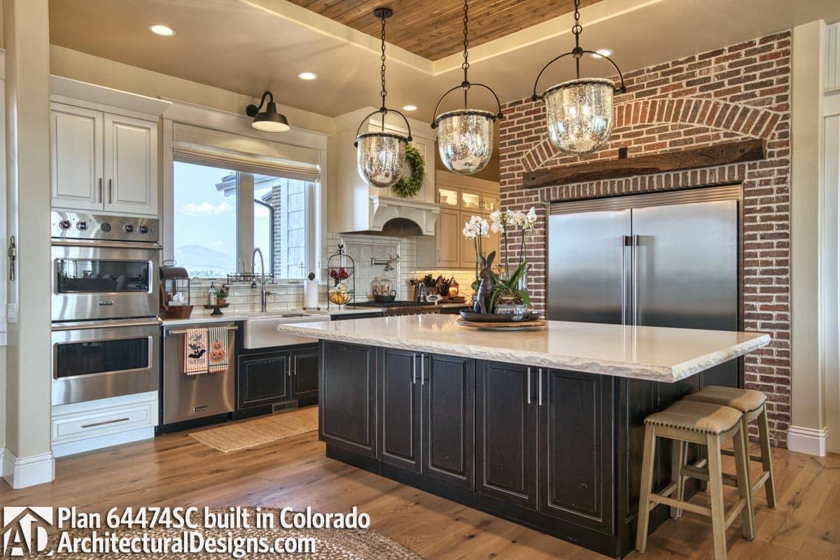Kitchen featuring a large island, farmhouse sink, stainless steel appliances, and brick accent wall with wood beam.