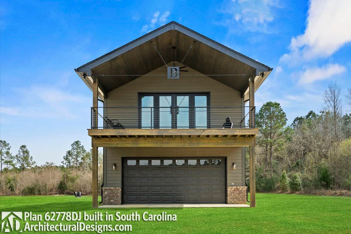 House plan exterior with a wide garage door on the lower level and a balcony with French doors above. Modern design with a gable roof.