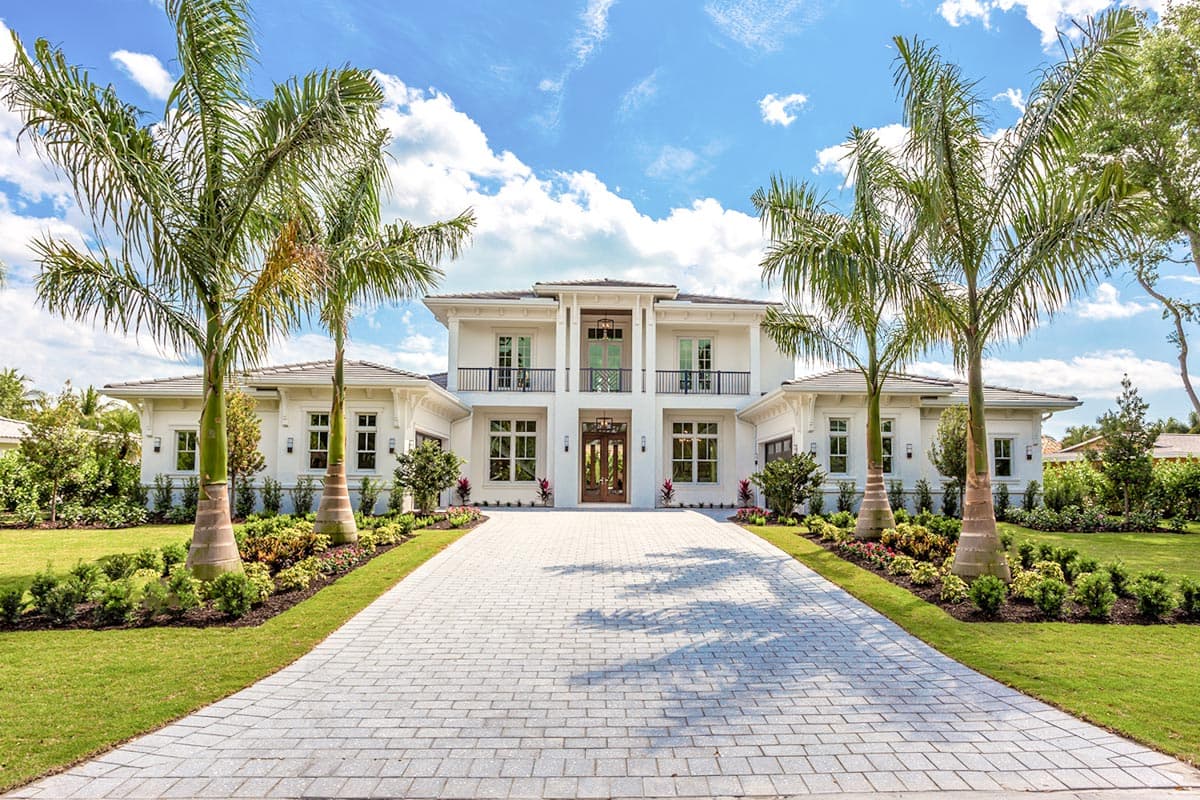 House plan exterior. Two-story, white stucco facade with a covered entry, balconies, and multiple gables. Driveway leads to the front door.