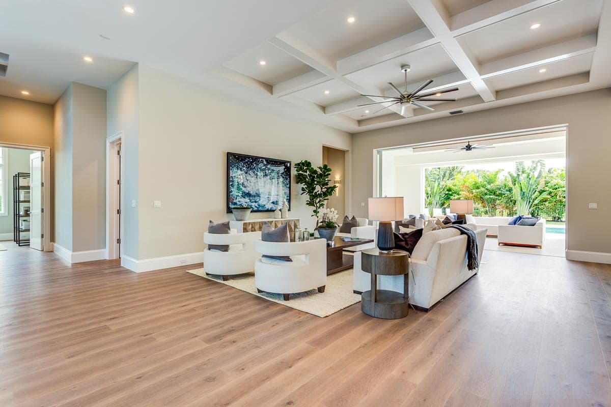 Living room with coffered ceiling, sofa, chairs, and view to outdoor patio with pool.