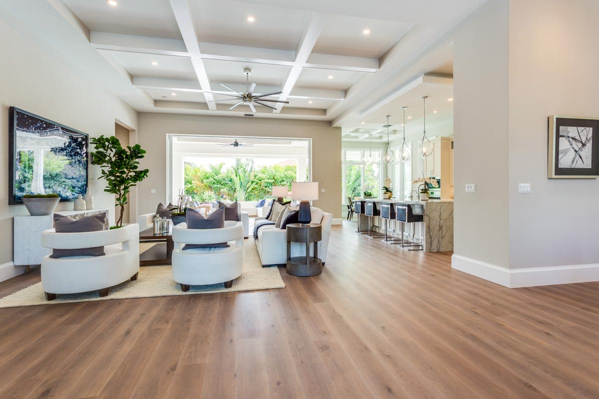 Open-concept living space with coffered ceiling, large windows to outdoor area, and kitchen island with bar seating.