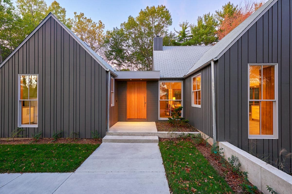 Modern house plan exterior with dark vertical siding, asymmetrical gables, and a large wooden front door.